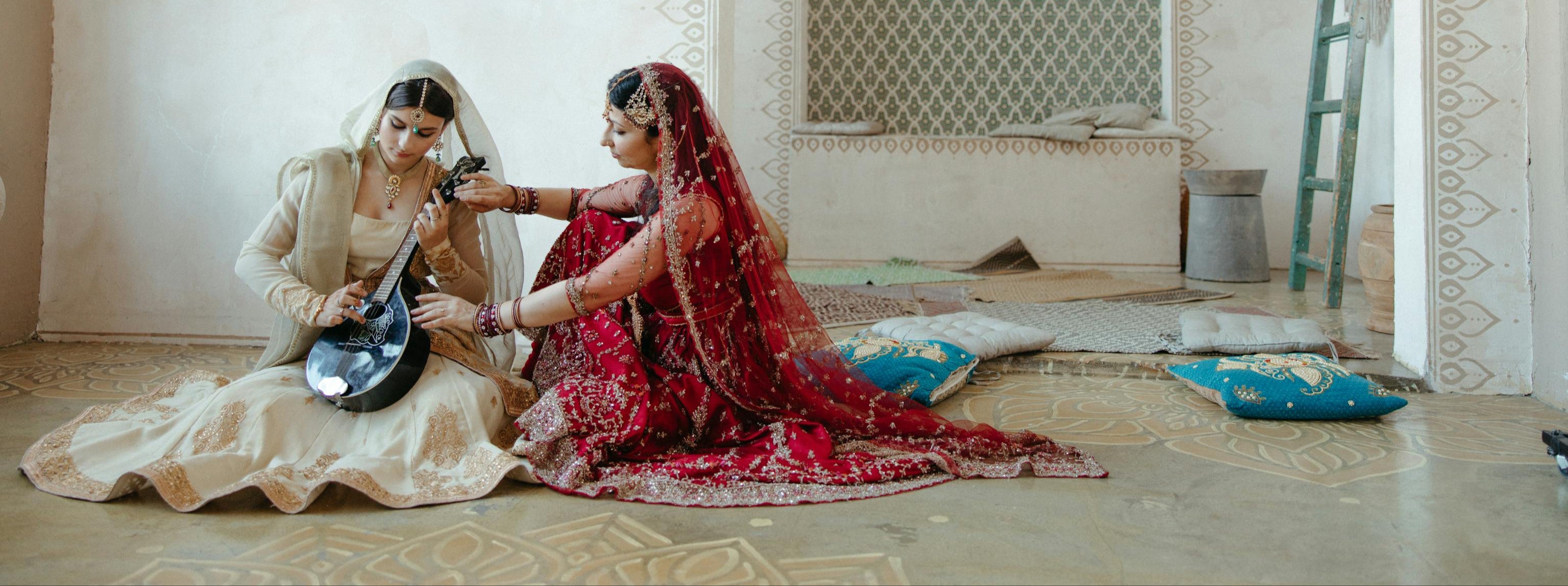 Two women in traditional attire sitting on a patterned floor with decorative elements.